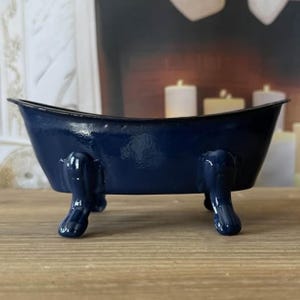 May include: A small, navy blue bathtub with claw feet. The miniature tub has a glossy finish and a curved rim. The tub is a decorative item, possibly for display or as a unique container.