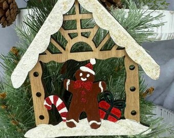 Peut inclure: Ornement de Noël en bois en forme de maison en pain d'épices. Il présente un bonhomme en pain d'épices, une canne en sucre et un cadeau emballé. Le toit est orné de blanc et l'ornement est suspendu à une boucle de ficelle.