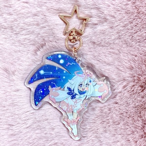 May include: A clear keychain with a holographic finish featuring a cartoon character with blue hair and a white dress. The character is surrounded by a blue and purple galaxy design. The keychain is attached to a gold star-shaped charm.