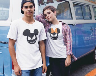 Puede incluir: Dos personas con camisetas blancas con un gráfico en blanco y negro de la cabeza de Mickey Mouse con una cara de Jack Skellington. La mujer lleva una camisa de cuadros sobre su camiseta y tiene un lazo en su camiseta. El hombre lleva una gorra de béisbol. Están de pie frente a una camioneta azul.