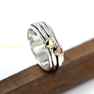 May include: A silver spinning ring with three hearts, one gold, one rose gold, and one silver.