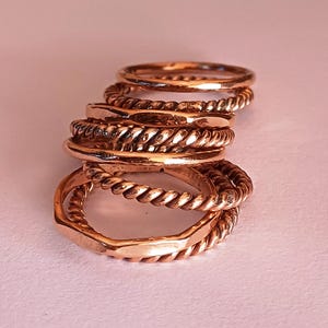K&ouml;nnte beinhalten: Ein Stapel aus f&uuml;nf goldfarbenen Ringen, einige mit einem gedrehten Seil-Design, andere mit einer glatten Oberfl&auml;che.