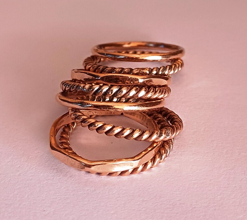 K&ouml;nnte beinhalten: Ein Stapel aus f&uuml;nf goldfarbenen Ringen, einige mit einem gedrehten Seil-Design, andere mit einer glatten Oberfl&auml;che.