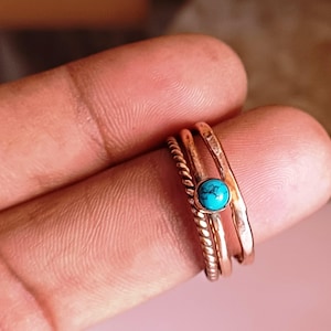 Pode incluir: Três anéis de ouro empilhados em um dedo. O anel superior tem uma pedra turquesa.