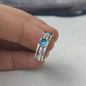 May include: A silver ring with three bands and a blue gemstone in the center.