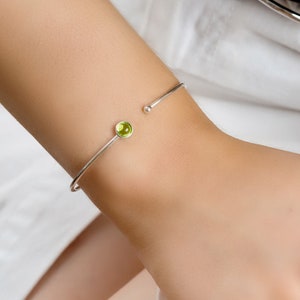 May include: A silver bangle bracelet with a single green gemstone set in the centre.