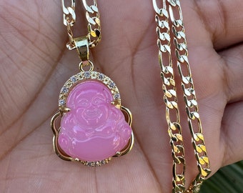 May include: A gold chain necklace with a pink, carved, and detailed Buddha pendant. The pendant is surrounded by small, clear stones.