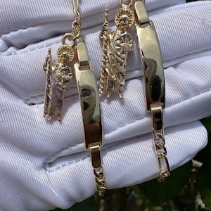 May include: Two gold chain bracelets with a saint charm and a nameplate charm. The charms are detailed and the chains are delicate.