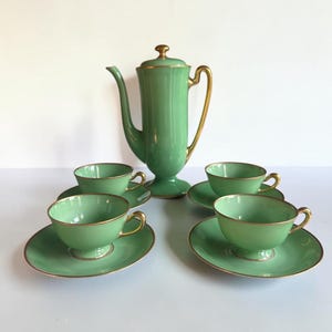 May include: A light green tea set consisting of a tall teapot with a lid and four matching teacups with saucers. Each piece features a smooth, solid light green finish accented with thin gold trim along the rims, handles, and base edges.