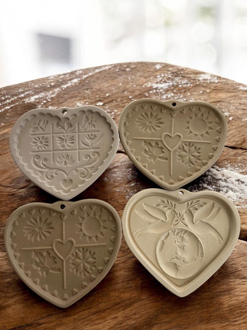 Puede incluir: Cuatro moldes de cer&aacute;mica en forma de coraz&oacute;n con varios dise&ntilde;os en relieve. Los moldes presentan motivos florales, solares, de copos de nieve y de palomas. Cada molde tiene un peque&ntilde;o agujero para colgar. Los moldes son beige.