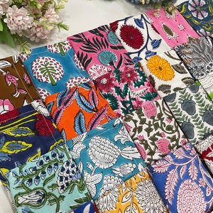 Può includere: Una collezione di quadrati di tessuto colorati e fantasia. I quadrati presentano disegni floreali e botanici in vari colori, tra cui rosa, blu, arancione e bianco. Il tessuto sembra essere cotone o un materiale simile, e l'estetica generale è luminosa e allegra.