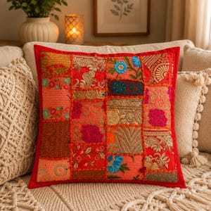 Puede incluir: Un cojín decorativo cuadrado con un vibrante diseño de patchwork compuesto por varios cuadrados de tela en tonos rojos, naranjas y dorados. La superficie está adornada con bordados intrincados, motivos florales, hilos dorados y costuras.