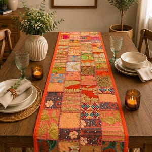 May include: A rectangular table runner featuring a patchwork design of various colorful fabric squares. The runner is decorated with intricate embroidery, small beads, and floral appliques in shades of orange, red, green, and blue.