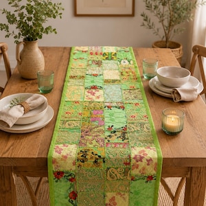 Peut inclure: Un chemin de table rectangulaire compos&eacute; d'un assemblage de carr&eacute;s de tissu verts. Le chemin pr&eacute;sente des broderies complexes, des motifs floraux et des accents de fils m&eacute;talliques dans des tons vert lime, &eacute;meraude et olive avec une bordure unie.