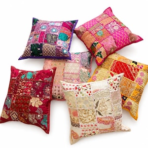 Puede incluir: Una colección de seis cojines cuadrados con diseños de patchwork hechos de diversas telas. Los cojines muestran una vibrante gama de colores que incluye rojo, rosa, morado, amarillo y crema, con detalles intrincados de bordado y lentejuelas.
