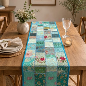 Peut inclure: Un chemin de table rectangulaire compos&eacute; d'un assemblage de carr&eacute;s de tissu dans des tons de bleu sarcelle, turquoise et vert. Le chemin est orn&eacute; de broderies florales et de motifs complexes, avec une bordure unie bleu vif.