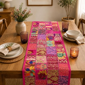 Peut inclure: Un chemin de table rectangulaire pr&eacute;sentant un motif patchwork vibrant compos&eacute; de divers carr&eacute;s de tissu rose, magenta et dor&eacute;. Le chemin est orn&eacute; de broderies complexes, de d&eacute;tails en fil m&eacute;tallique et de petites perles blanches sur toute la surface.