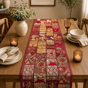 Peut inclure: Un chemin de table rectangulaire pr&eacute;sentant un motif patchwork compos&eacute; de divers carr&eacute;s de tissu rouge et dor&eacute;. Le chemin est orn&eacute; de broderies complexes, de d&eacute;tails en fil m&eacute;tallique et de petits miroirs r&eacute;fl&eacute;chissants sur tout le tissu.