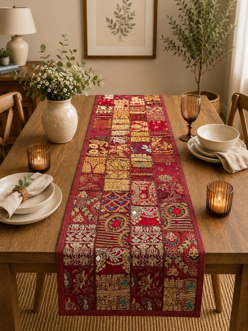 Peut inclure: Un chemin de table rectangulaire pr&eacute;sentant un motif patchwork compos&eacute; de divers carr&eacute;s de tissu rouge et dor&eacute;. Le chemin est orn&eacute; de broderies complexes, de d&eacute;tails en fil m&eacute;tallique et de petits miroirs r&eacute;fl&eacute;chissants sur tout le tissu.