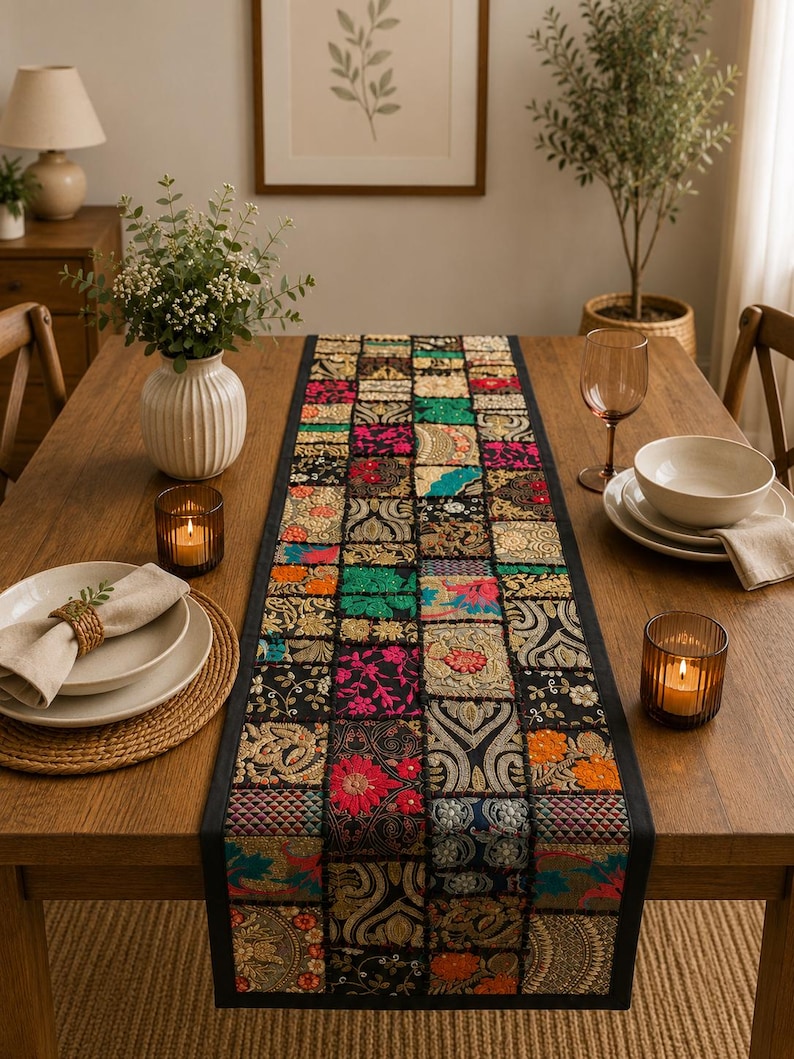 Peut inclure: Un chemin de table rectangulaire compos&eacute; d'un assemblage de carr&eacute;s de tissu. Chaque carr&eacute; pr&eacute;sente des broderies complexes, des d&eacute;tails en fil m&eacute;tallique et des couleurs vives comme le fuchsia, le vert, l'orange et l'or sur fond noir.