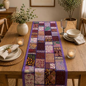Peut inclure: Un chemin de table rectangulaire compos&eacute; d'un assemblage de carr&eacute;s de tissu aux tons violets, roses, dor&eacute;s et bordeaux. Le chemin de table pr&eacute;sente une bordure violette unie et des motifs brod&eacute;s, floraux et des textures m&eacute;talliques.