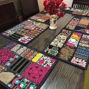 Peut inclure: Une table à manger en bois avec des sets de table brodés colorés. Les sets de table présentent un motif patchwork avec divers motifs et couleurs, dont le rose, l'or et le bleu. Un vase de roses rouges est au centre de la table.