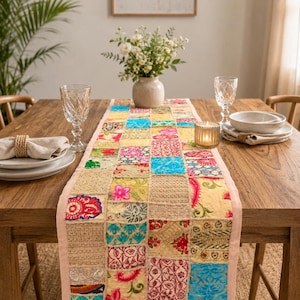Peut inclure: Un chemin de table rectangulaire compos&eacute; d'un assemblage de carr&eacute;s de tissus aux couleurs vives, notamment bleu, rose, jaune et dor&eacute;. Le chemin pr&eacute;sente des broderies complexes, des motifs floraux et des d&eacute;tails en fils m&eacute;talliques.