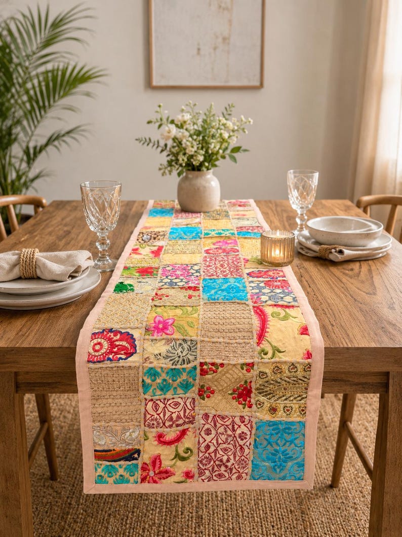 Peut inclure: Un chemin de table rectangulaire compos&eacute; d'un assemblage de carr&eacute;s de tissus aux couleurs vives, notamment bleu, rose, jaune et dor&eacute;. Le chemin pr&eacute;sente des broderies complexes, des motifs floraux et des d&eacute;tails en fils m&eacute;talliques.