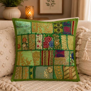 May include: A square throw pillow featuring a patchwork design of various green fabric panels. The surface is decorated with intricate embroidery, gold-toned metallic thread, sequins, and floral patterns. The pillow is framed by a solid green border.