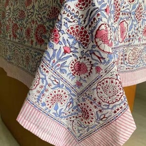 May include: A white tablecloth with a pink and blue floral pattern. The tablecloth has a pink and white striped border.