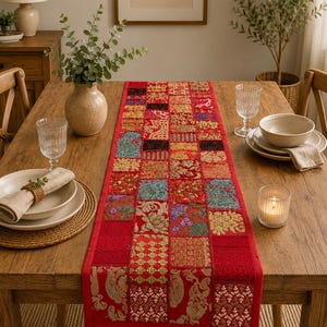 Peut inclure: Un chemin de table rectangulaire compos&eacute; d'un patchwork de carr&eacute;s de tissu rouge. Chaque carr&eacute; pr&eacute;sente des motifs brod&eacute;s distincts, des ornements floraux et des accents de fil dor&eacute; m&eacute;tallique, cr&eacute;ant une surface textur&eacute;e et vari&eacute;e.