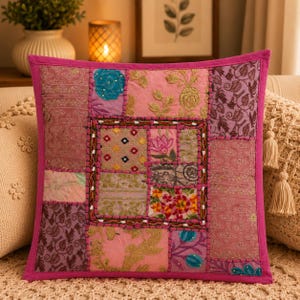 May include: A square throw pillow featuring a patchwork design of various pink, purple, and gold fabric panels. The surface displays intricate embroidery, floral patterns, and decorative stitching, framed by a solid pink border on all four sides.