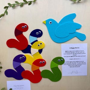 Peut inclure: Un ensemble de contes en feutrine avec six vers de terre ondulants colorés et un oiseau bleu. Les vers sont rouges, violets, verts, jaunes et bleus. L'ensemble comprend une carte imprimée avec le titre "6 Wiggly Worms" et le texte de l'histoire.