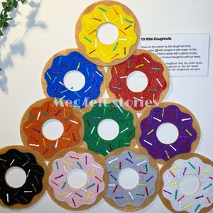 Puede incluir: Diez donuts de fieltro con chispas de colores dispuestos en forma de pirámide. Los donuts son de varios colores, incluyendo amarillo, azul, rojo, naranja, verde, morado, negro, rosa y gris. El texto "10 little Doughnuts" es visible en una tarjeta blanca.