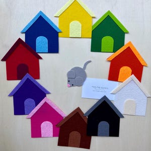 May include: A circular arrangement of felt houses in a variety of colours, including blue, yellow, green, red, purple, pink, brown, black, and white. A grey felt mouse and a card with text are in the centre.