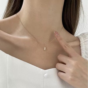 May include: A delicate gold chain necklace with a small, rectangular pendant featuring a clear stone.