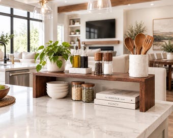 May include: A dark wood countertop shelf holding a white ceramic planter with a green plant, a marble tray with oil and vinegar bottles, two glass spice grinders, a white marble utensil crock with wooden spoons, and two stacked books.