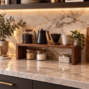 May include: A dark wood countertop shelf holding a black gooseneck kettle, a black coffee dripper, two light-coloured mugs, and two glass jars with wood lids containing coffee beans and sugar. A third glass jar with a wood lid sits below.