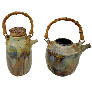 May include: Two ceramic vessels with bamboo handles and spouts. The taller vessel features a textured cork stopper. Both items display a mottled glaze in shades of tan, brown, and blue, with a smooth, rounded body shape and visible drip patterns.