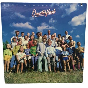 May include: Album cover for Quarterflash's "Take Another Picture." The cover features a group of mannequins dressed in various outfits, set against a blue sky with clouds. The band's name is in a stylized font.