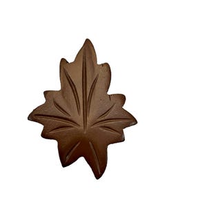 May include: A brown maple leaf-shaped ornament with a carved design. The ornament is made of a textured material and has a rustic look.