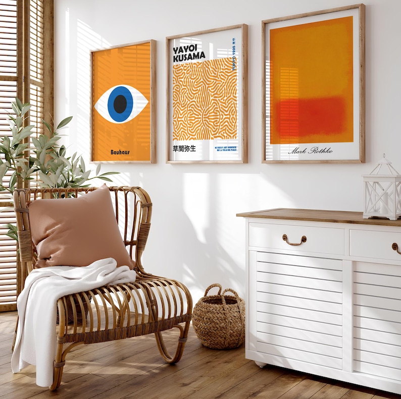 Puede incluir: Tres impresiones de arte enmarcadas en una pared blanca. La impresi&oacute;n de la izquierda es naranja con un ojo azul y el texto "Bauhaus". La impresi&oacute;n del medio es naranja con un patr&oacute;n blanco y naranja y el texto "Yayoi Kusama" y "草間彌生". La impresi&oacute;n de la derecha es naranja con un rect&aacute;ngulo rojo y el texto "Mark Rothko".