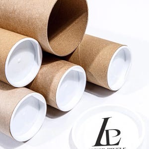 May include: Five brown cardboard tubes with white end caps stacked on top of each other. A white round sticker with the text "Luxor Pixels" and a black stylized "LP" logo is in the foreground.