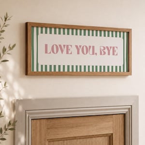 May include: A rectangular wall sign with a wooden frame featuring a white center panel with the pink text LOVE YOU, BYE. The background behind the text consists of vertical green and white stripes, creating a distinct contrast within the frame.