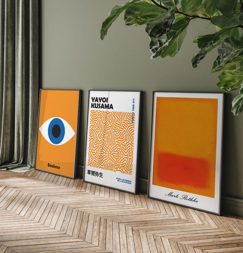 Puede incluir: Tres impresiones de arte enmarcadas con un dise&ntilde;o minimalista. La impresi&oacute;n de la izquierda presenta un ojo azul sobre un fondo amarillo con el texto "Bauhaus". La impresi&oacute;n del medio presenta un patr&oacute;n abstracto blanco y naranja con el texto "Yayoi Kusama" y texto japon&eacute;s. La impresi&oacute;n de la derecha presenta un degradado amarillo y naranja con el texto "Mark Rothko".
