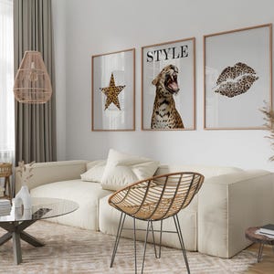 May include: Three framed prints with a leopard print theme. The prints feature a star, a leopard with the word "STYLE" above it, and a leopard print lip. The prints are hanging on a white wall above a white couch with a brown wicker chair.