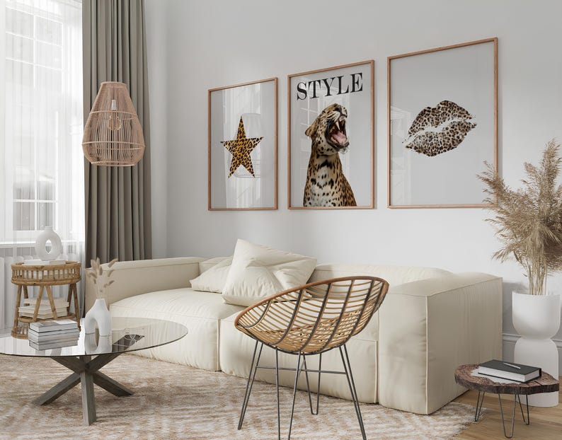 May include: Three framed prints with a leopard print theme. The prints feature a star, a leopard with the word "STYLE" above it, and a leopard print lip. The prints are hanging on a white wall above a white couch with a brown wicker chair.