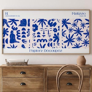 May include: A framed art print with a collage of blue abstract shapes on a pale pink backdrop. The print includes the text "Papiers Découpés" and "Matisse Paris-49". The artwork is displayed above a wooden chest of drawers.