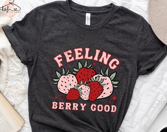 May include: A dark gray t-shirt with a graphic of strawberries and the text "Feeling Berry Good".