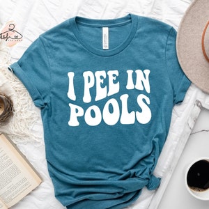 May include: A teal blue t-shirt with the text "I PEE IN POOLS" in white, retro-style lettering.